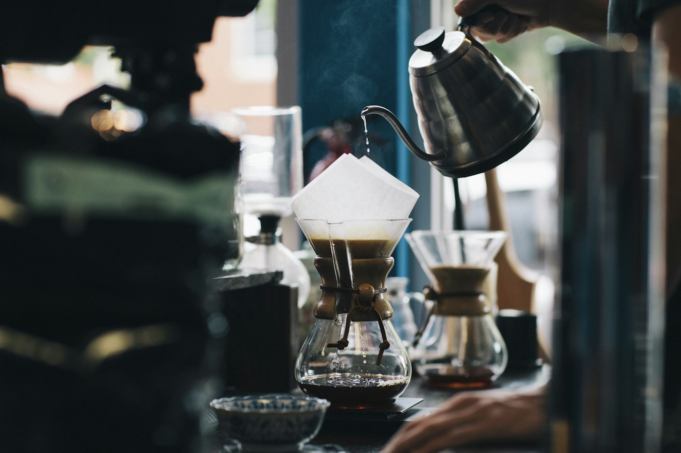 A barista pouring water from a gooseneck kettle into a pour-over brewer