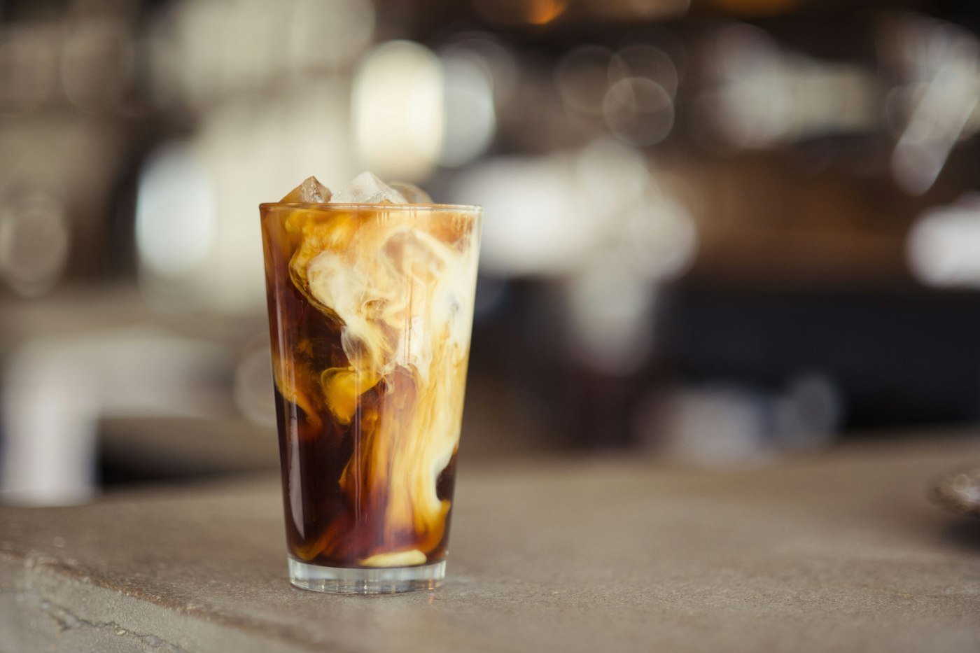 An iced coffee with milk swirling through it on a café counter