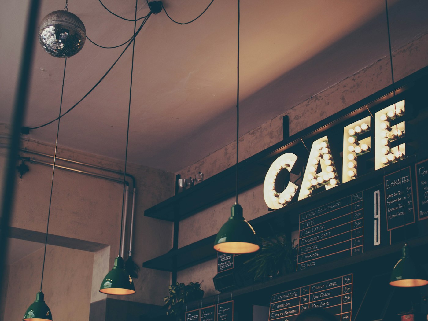 A café interior with pendant lights, chalkboard menus and a lit CAFE sign