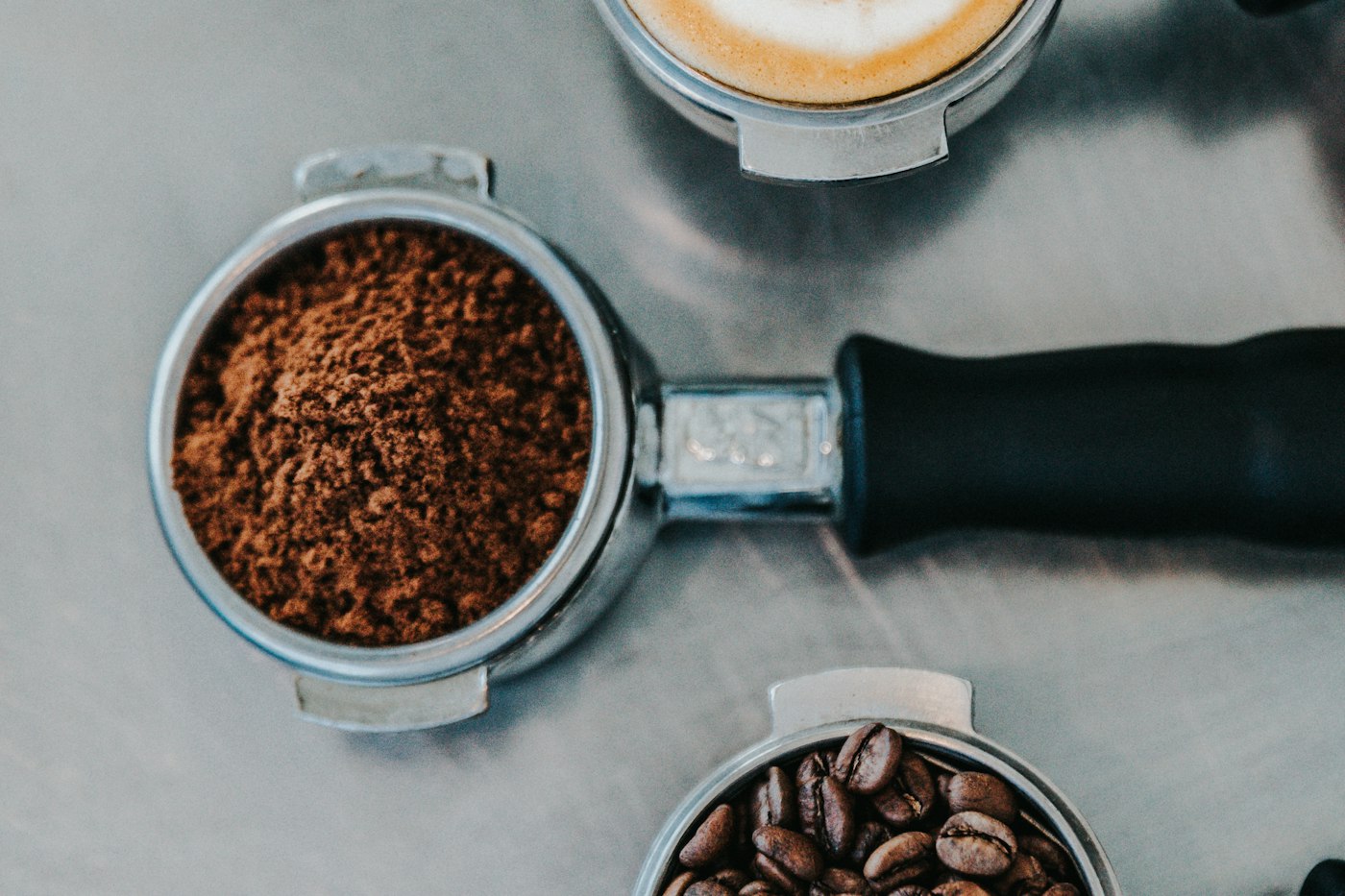 A portafilter of freshly ground coffee beside a cup of whole beans